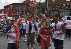 A jubilant group of Ottawa Pride parade participants wearing PIPSC t-shirts with rainbows, waving flags with big smiles on their faces.