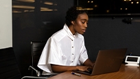 A woman sits at a table and works at a laptop. 